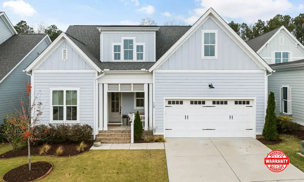 A modern new construction home with light blue siding, a two-car garage, and a front porch, highlighting the structural quality covered under comprehensive new home warranties.