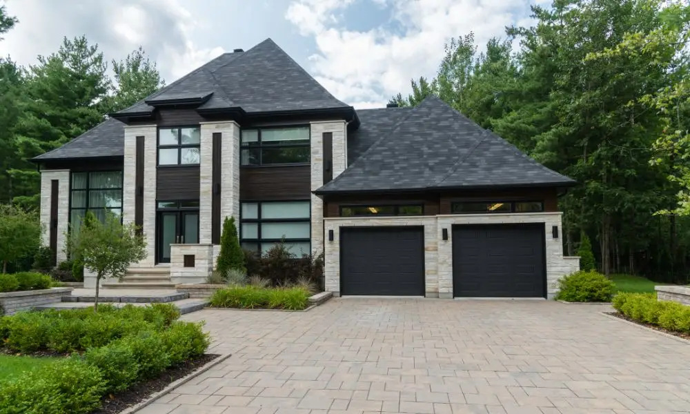 Modern luxury estate representing premium Franklin houses for sale, featuring a light stone and dark wood exterior, two-car garage, paved driveway, and lush green landscaping under a cloudy sky.